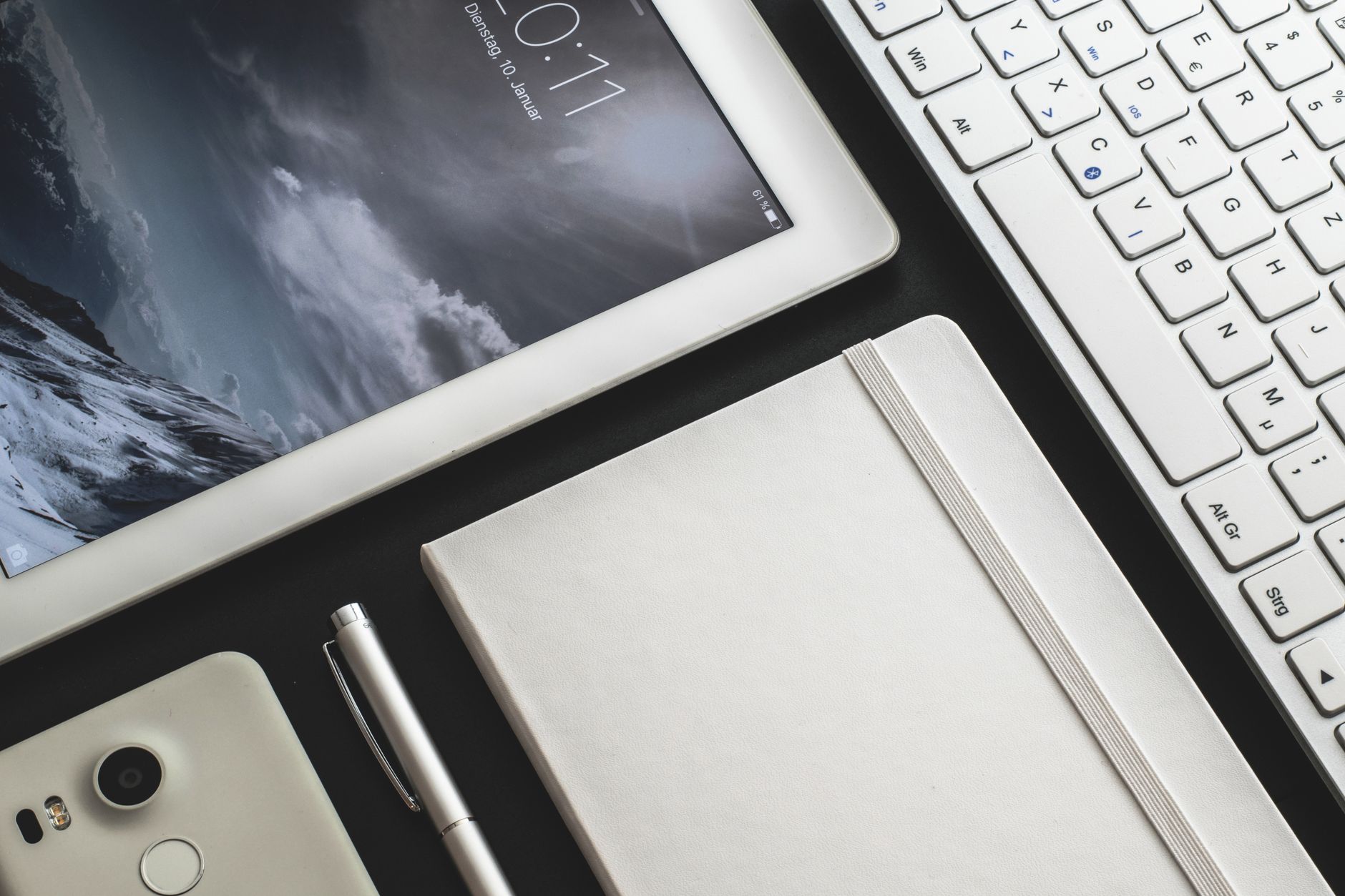 Overhead view of a modern desk setup featuring a tablet, smartphone, keyboard, and notebook.