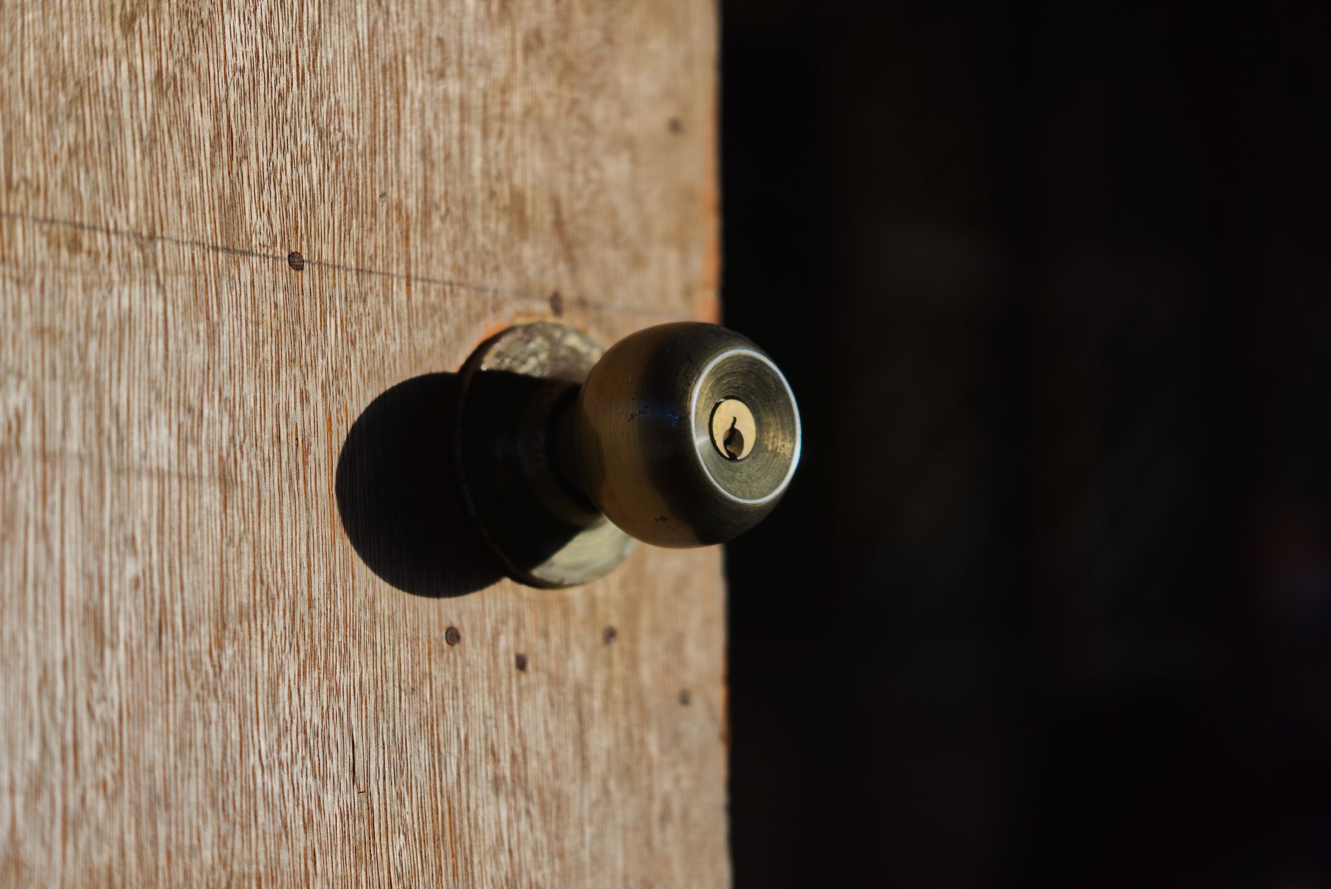 Detailed close-up of a metal door knob on a textured wooden surface with shadow play.