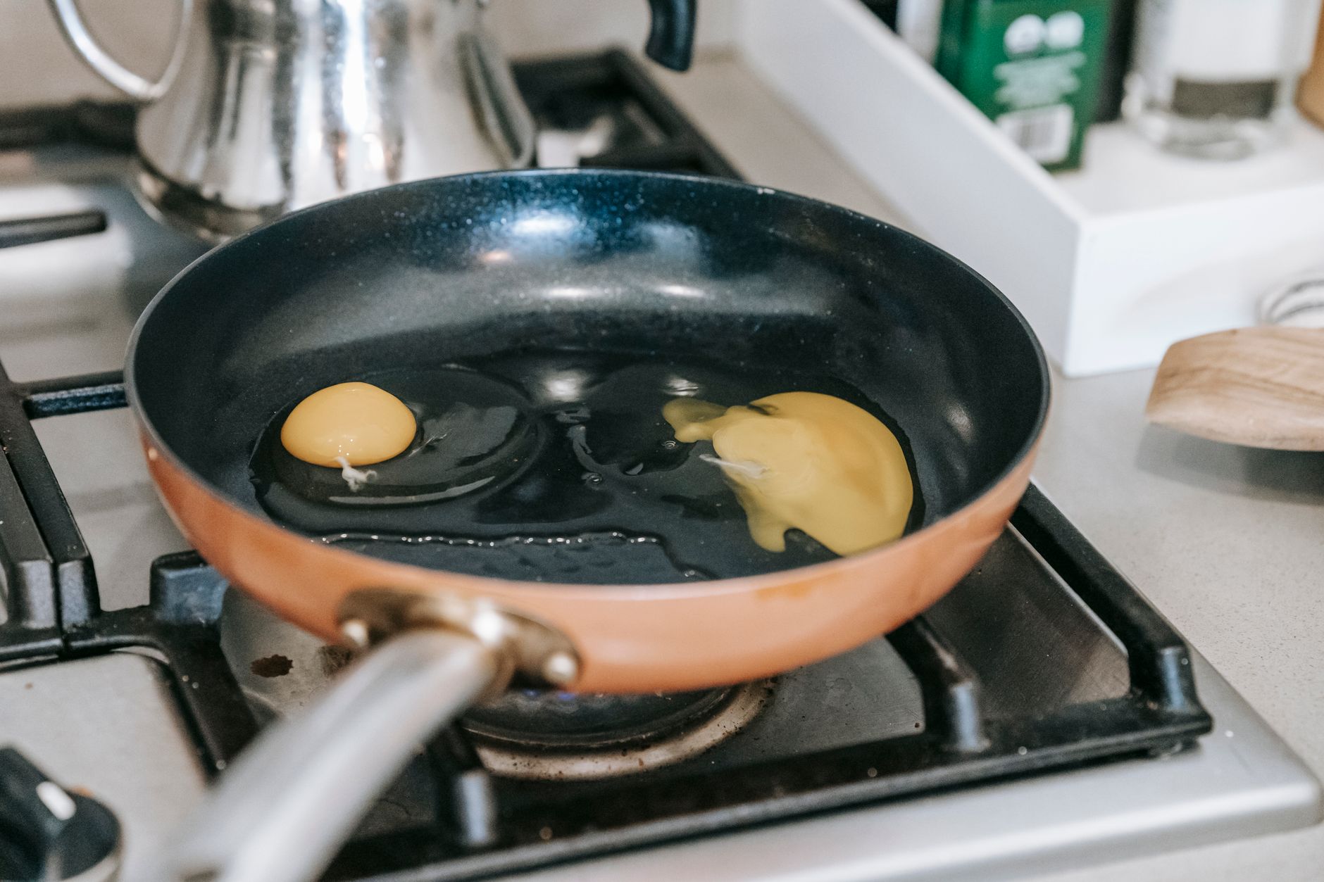 Chicken eggs with yellow yolks frying on pan on gas cooker near kettle in light kitchen with various appliances in apartment