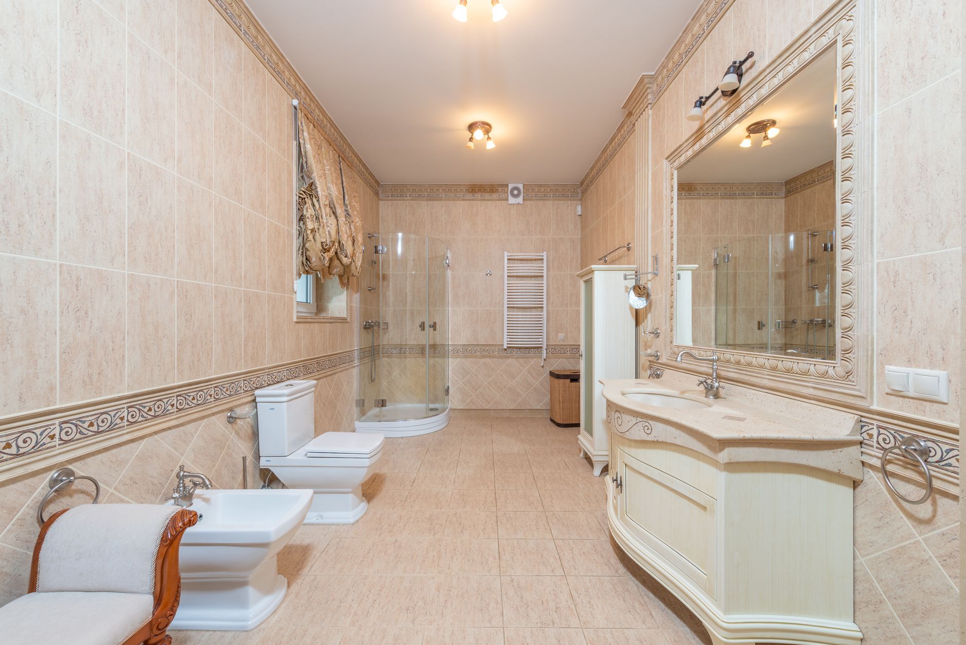 Spacious luxury bathroom featuring beige tiles, elegant furnishings, and modern fixtures.
