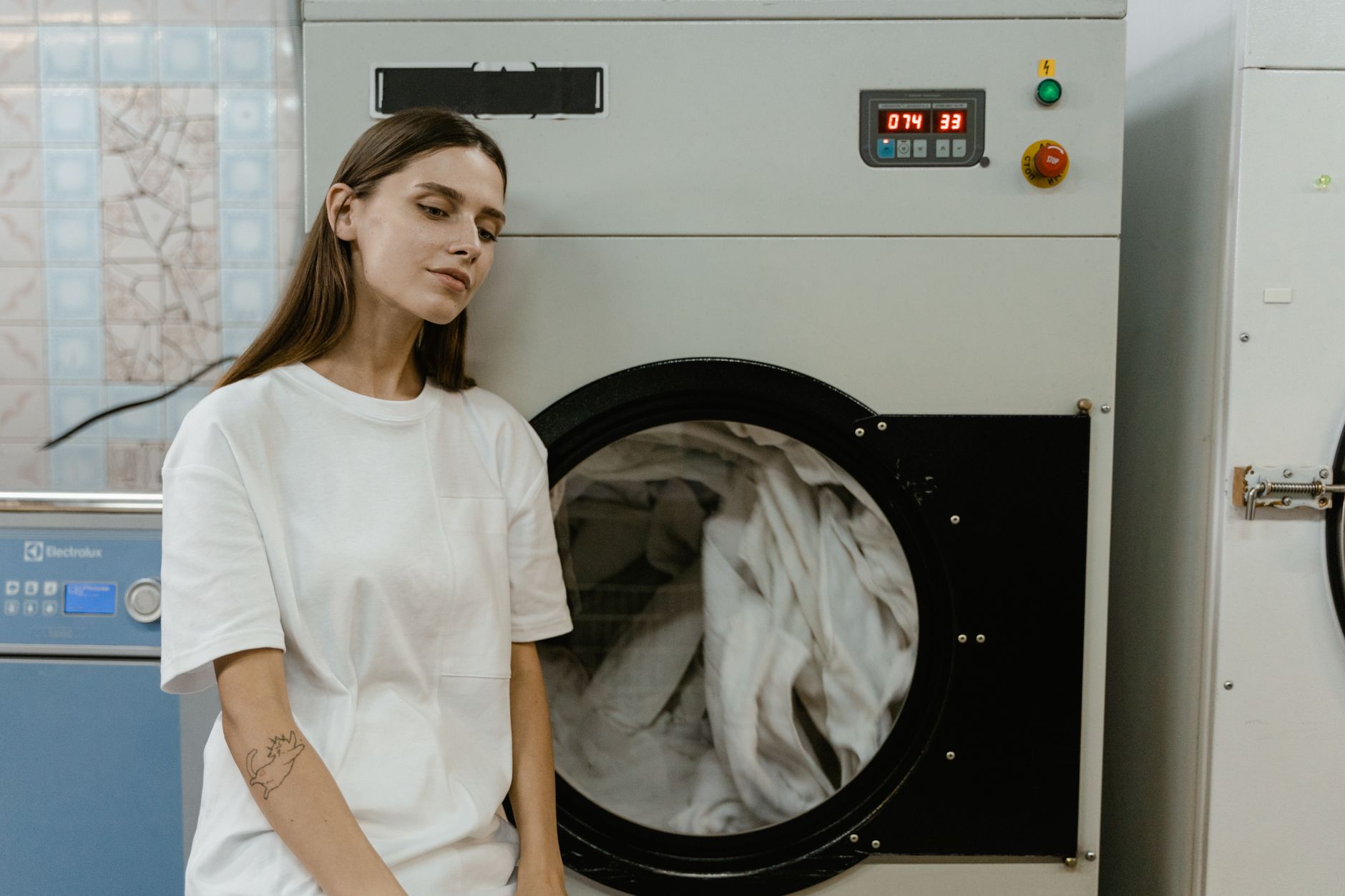 A woman in a laundry facility standing by a washing machine, contemplating the process.