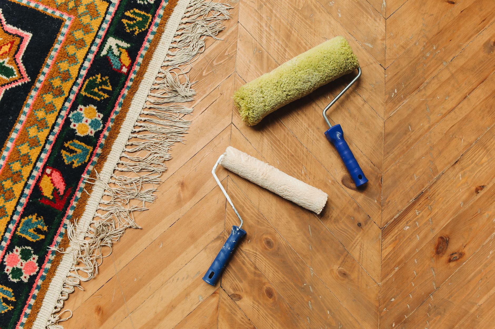 Two paint rollers on a wooden floor next to a colorful rug, symbolizing home renovation.