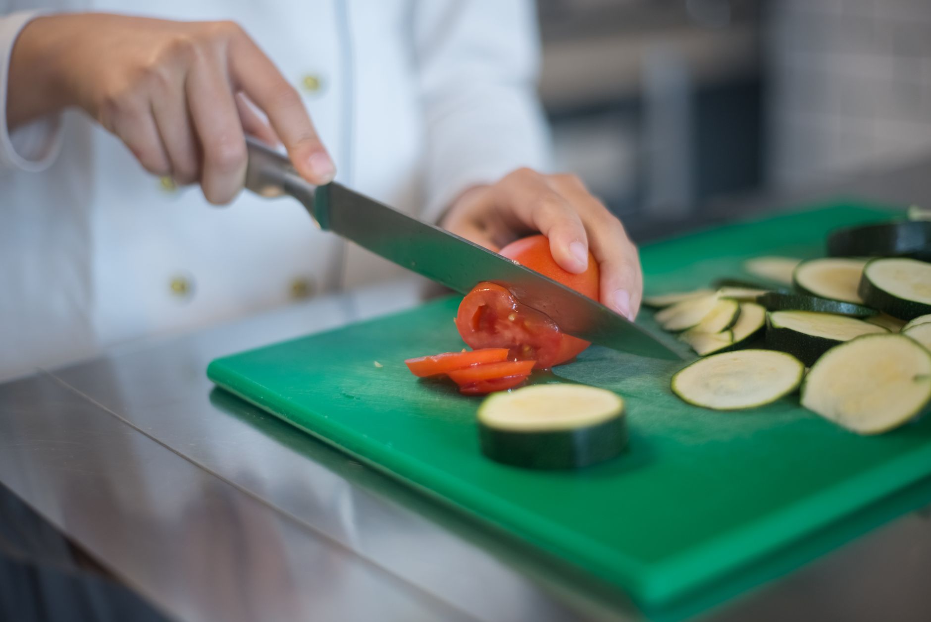Chef precisely slices tomato and zucchini on green board, enhancing culinary presentation.