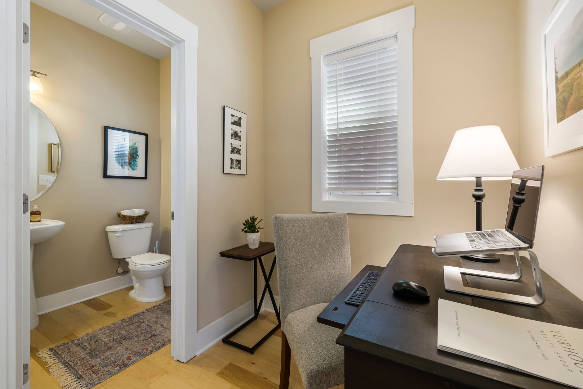 Compact home office with laptop setup and adjacent bathroom, bright and modern.