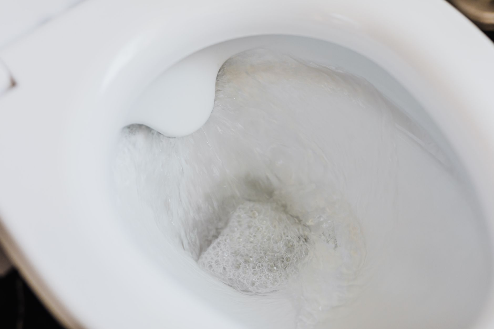 High angle of clean white ceramic toilet bowl with flushing foamy water in bathroom