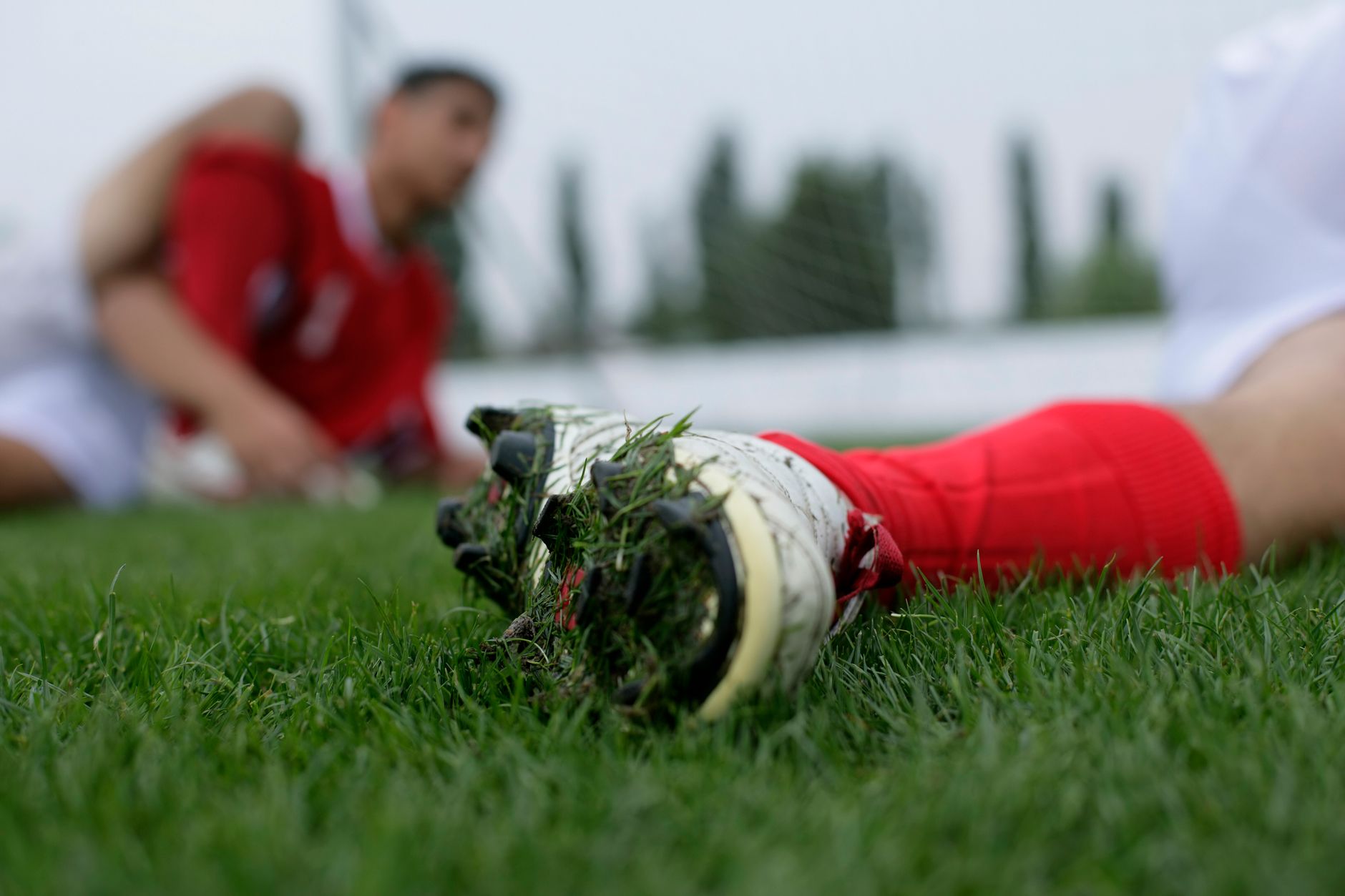 Focused shot of a soccer player's cleat on a grassy field with a teammate in the background.
